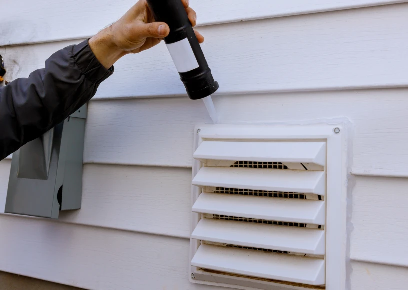 Hand using caulk on wall vent